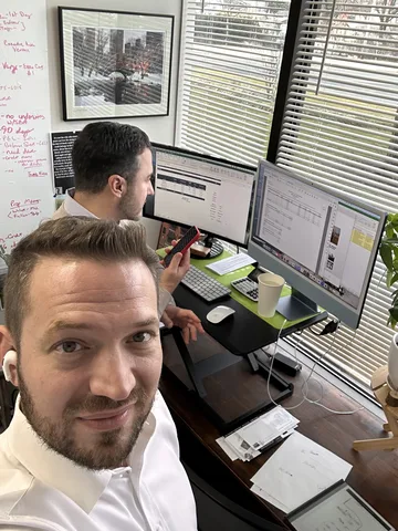 Bruce Elia Jr. taking a selfie at his desk while reviewing listings with a teammate